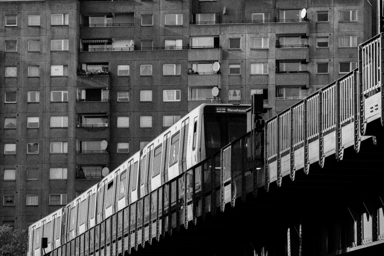 Black-and-white photo of a U-Bahn train on an elevated track in front of a Berlin apartment block
